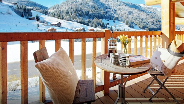 A wooden deck with a table and chairs, overlooking a snowy mountain landscape. - Chalet Le Mousqueton - ski base for 14 spa & mountain views - OVO Network (La Clusaz)