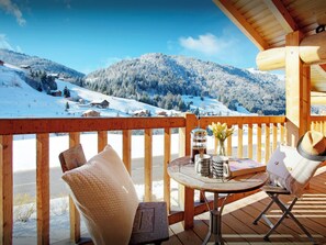 Une terrasse en bois avec une table et des chaises, offrant une vue sur un paysage montagneux enneigé.
