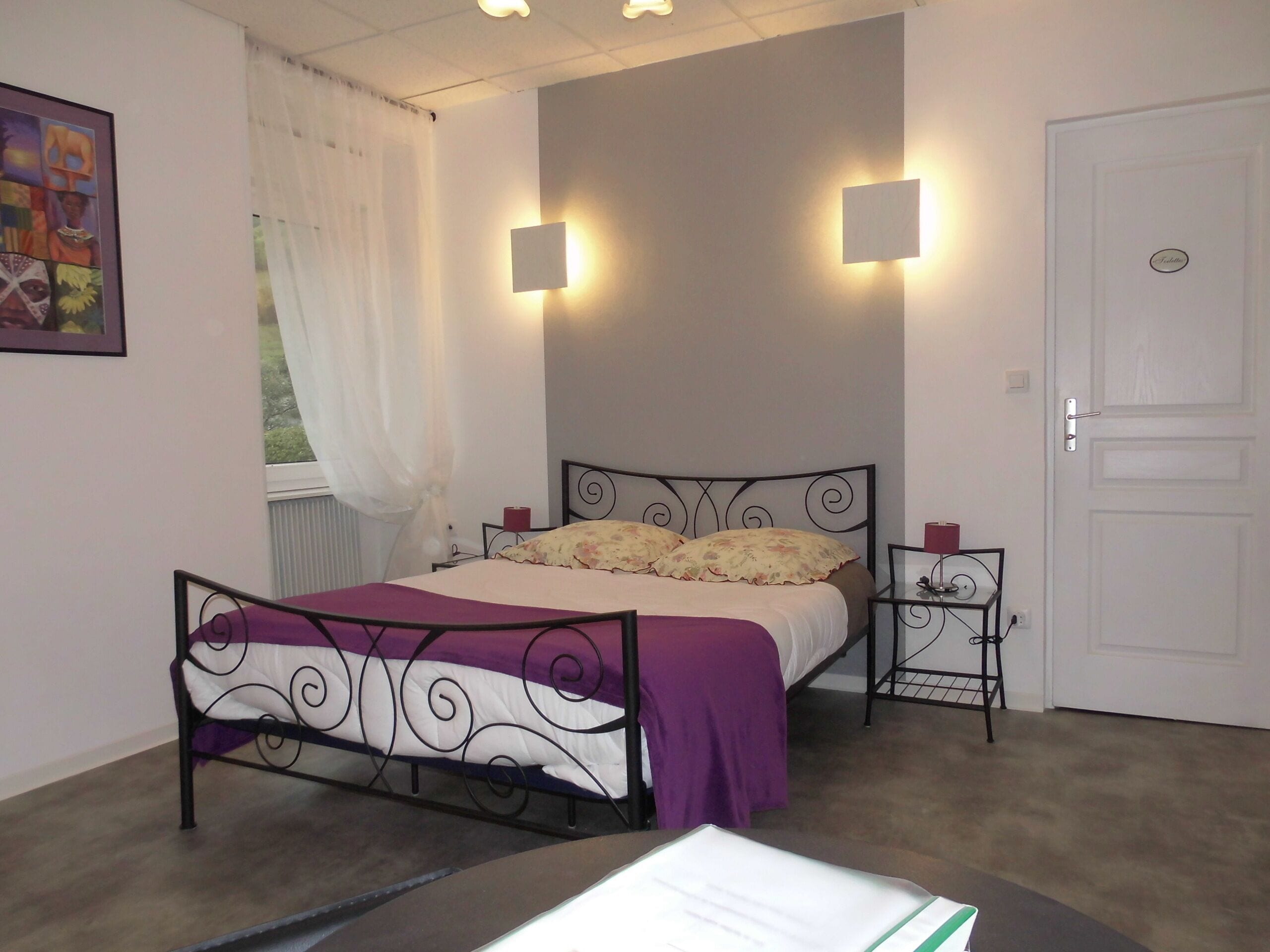 Un dormitorio con cama, mesitas de noche, una ventana con cortinas y una puerta.