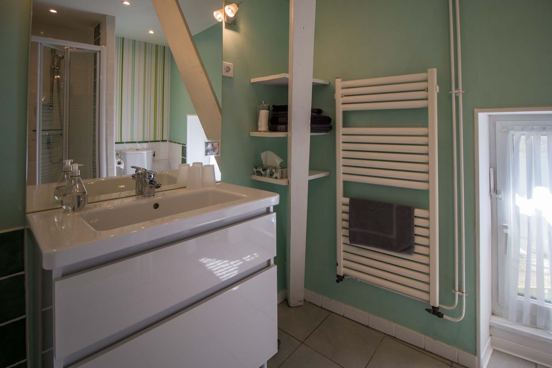 Baño con tocador blanco, espejo, ducha y toallero.