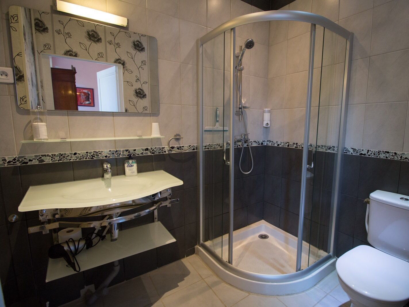 A modern bathroom with a curved glass shower enclosure, a white sink with a marble countertop, and a toilet.