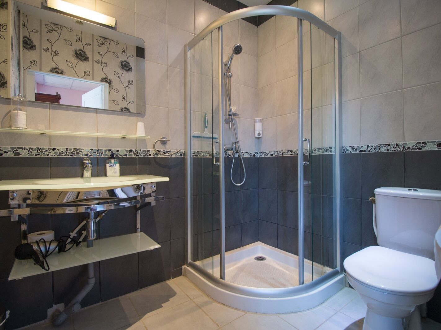 Une salle de bain moderne avec une douche à parois de verre, des toilettes blanches et un meuble-lavabo doté d’un miroir et d’étagères.