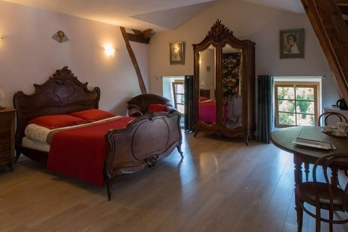 Ein Schlafzimmer mit einem großen Bett, einer Holzkommode, einem Spiegel und einem Esstisch mit Stühlen.