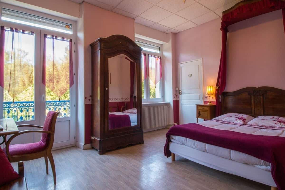 Ein Schlafzimmer mit einem Himmelbett, einem Holzstuhl, einem Schreibtisch und einem großen Spiegel.