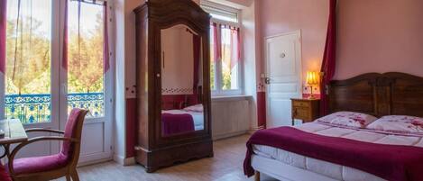 A bedroom with a four-poster bed, a wooden chair, a desk, and a large mirror.