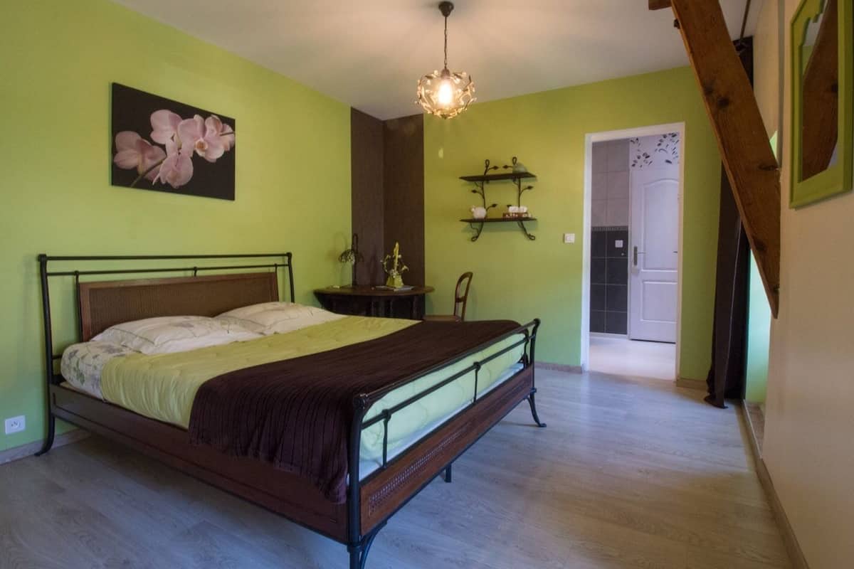 Ein Schlafzimmer mit einem Bett, einem Nachttisch, einem Sessel, einer Hängeleuchte und einer Tür zu einem anderen Raum.
