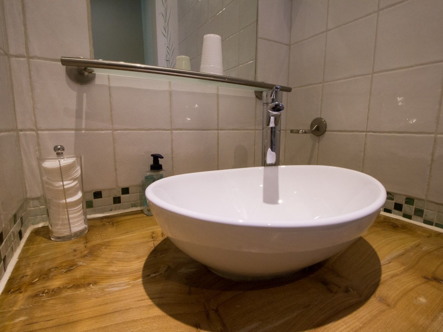 Un baño con un lavamanos grande de color blanco, un dispensador de jabón de vidrio y un perchero de metal para toallas.