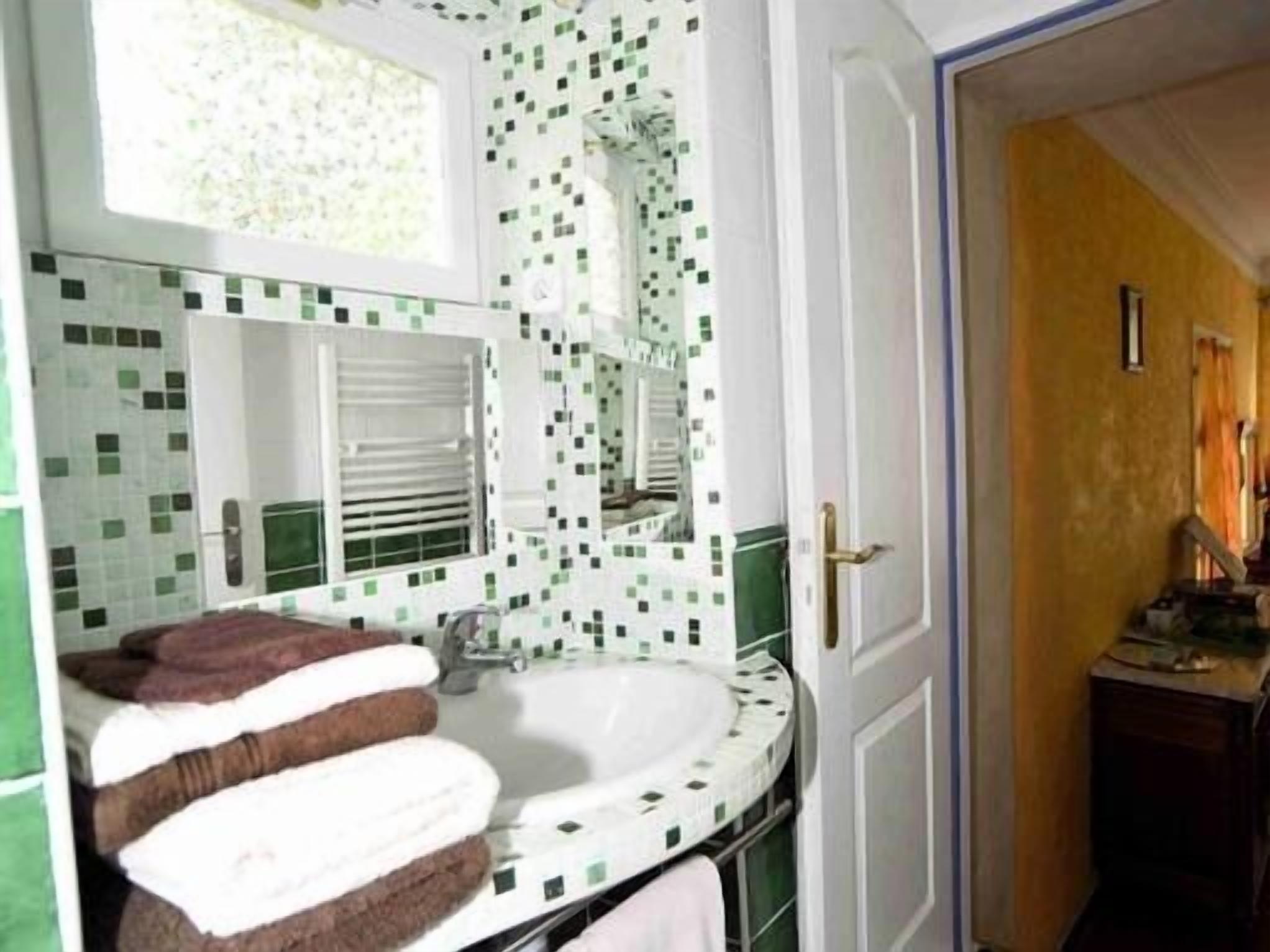 A bathroom with a white sink, green and white mosaic tiles, a mirror, and a towel rack with striped towels.