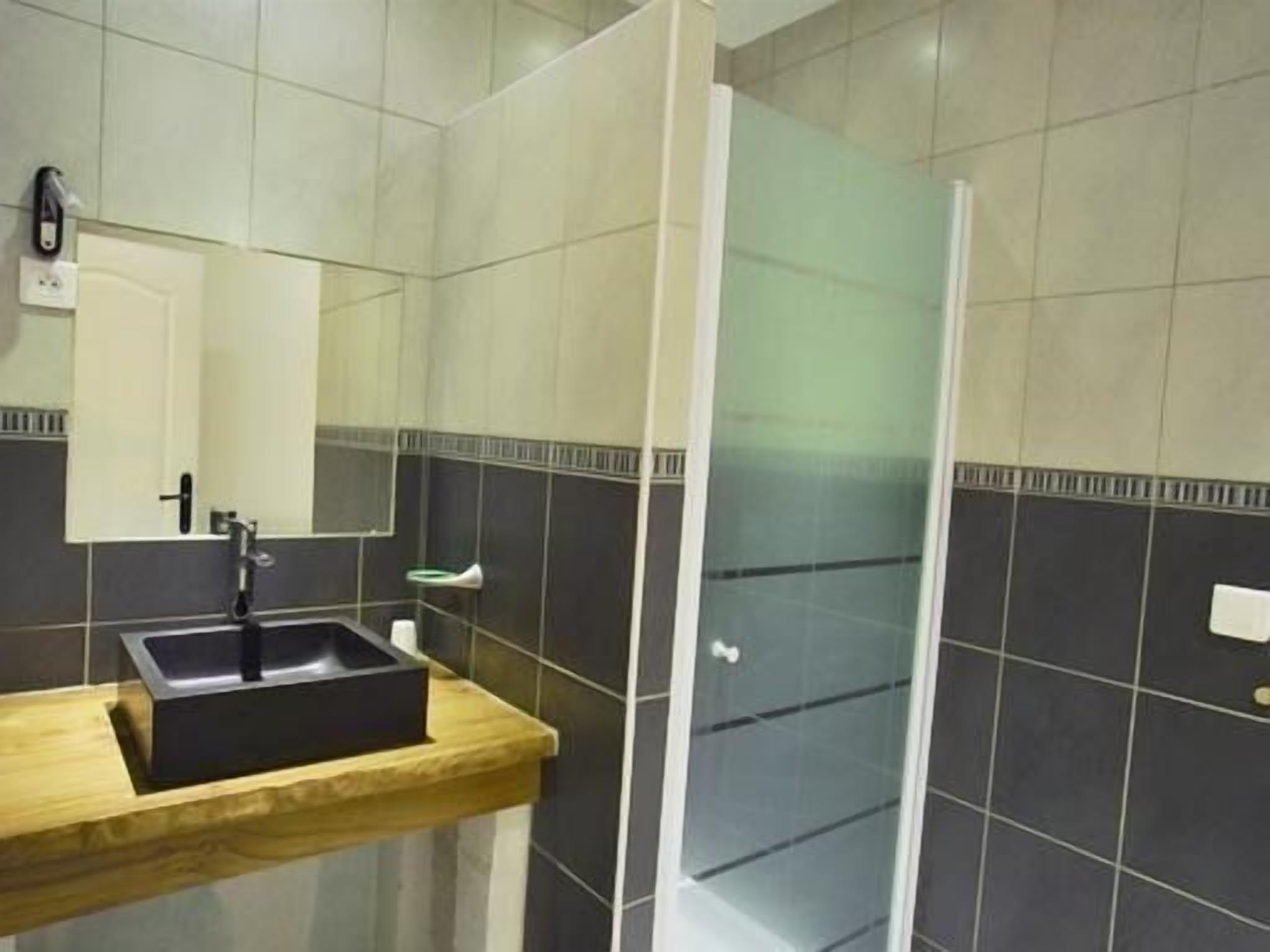 Un baño con tocador de madera, lavamanos negro, espejo y cabina de ducha de vidrio.