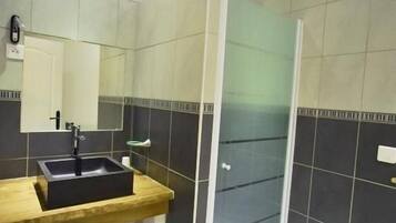 Un baño con tocador de madera, lavamanos negro, espejo y cabina de ducha de vidrio.