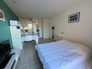 A compact hotel room with a bed, a small kitchenette, a dining area, and a TV.