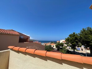A coastal residential area with terracotta roof tiles, a clear blue sky, and a view of the sea.