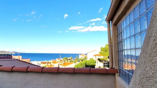 A coastal view from a balcony with a clear sky, overlooking a town with buildings and the sea.