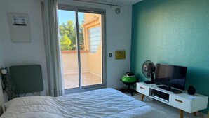 A bedroom with a bed, a TV, a fan, and a sliding door to a balcony.