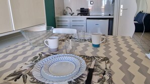 A dining area with a table set for two, a kitchen in the background, and a door leading to another room.