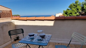 A small outdoor table with chairs, a tiled floor, and a view of the sea.