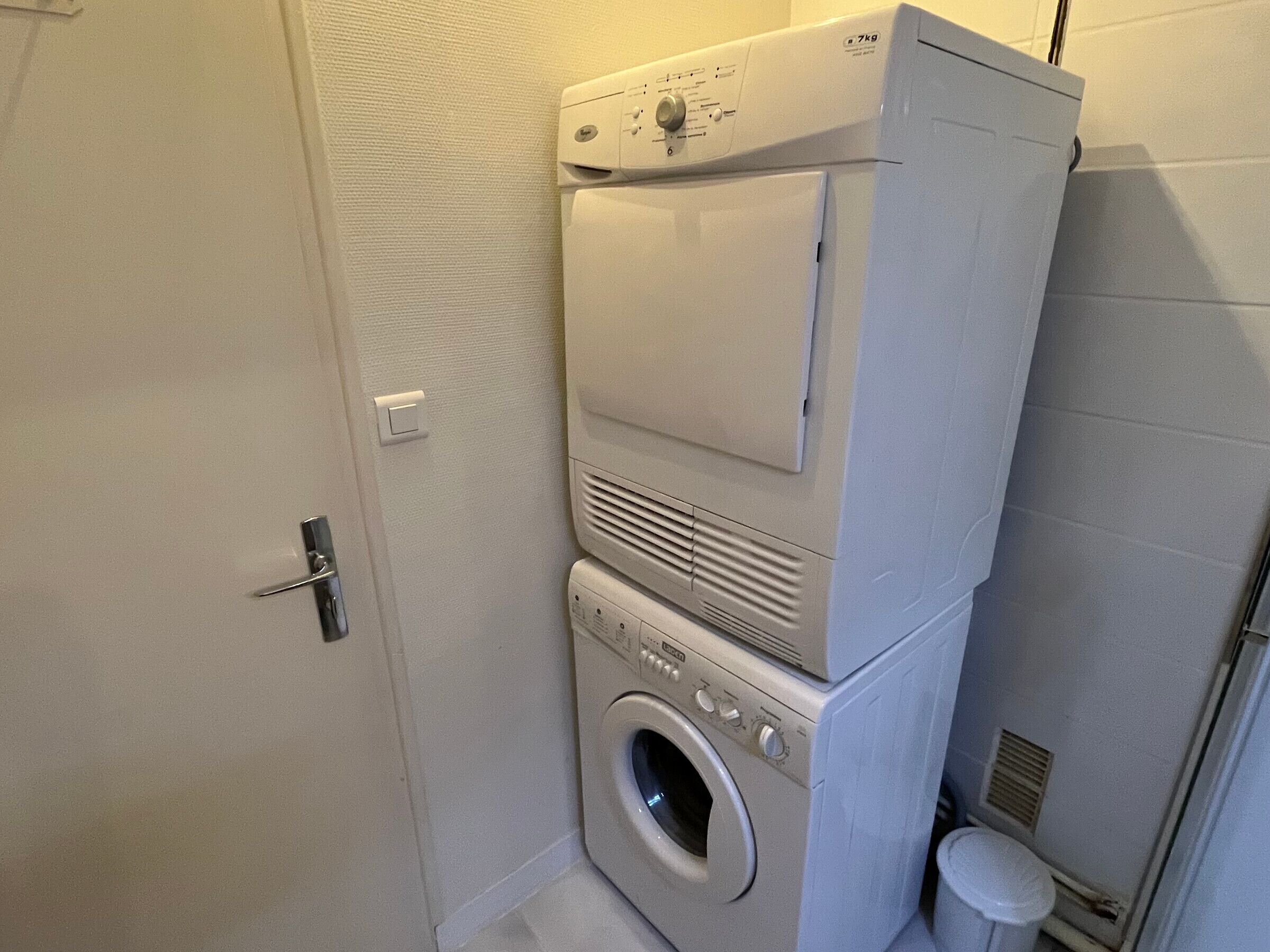A compact laundry room with a front-loading washer and dryer, a small sink, and a towel rack.