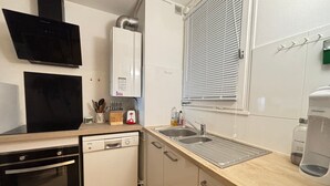Een kleine keuken met een vaatwasser, oven en een spoelbak met een raam erboven.