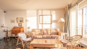 Un salón espacioso con un sofá color beige, sillas de mimbre, una mesa de centro de madera y un piano.