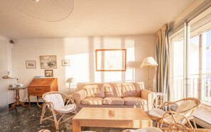 A spacious living room with a beige sofa, wicker chairs, a wooden coffee table, and a piano.