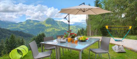 Un área de comedor al aire libre con mesa, sillas y una sombrilla, con vistas a un paisaje montañoso.