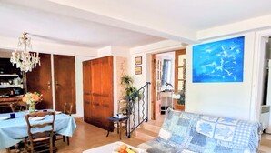 A living room with a sofa, a dining table with chairs, a chandelier, and a large painting on the wall. - T3 Apartment with garden in Banyuls, parking included (Banyuls-sur-Mer)