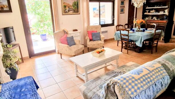 A living room with a sofa, armchairs, a coffee table, a dining table with chairs, a chandelier, and a television. - T3 Apartment with garden in Banyuls, parking included (Banyuls-sur-Mer)