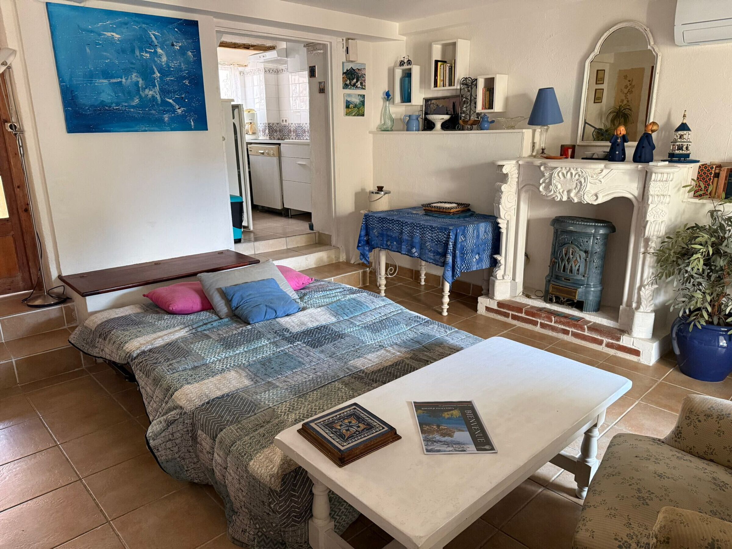 A cozy bedroom with a bed, bedside table, and a view of the kitchen.