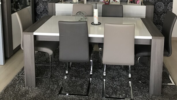 A dining area with a modern table and chairs, a patterned wallpaper, and a mirror above the table. - Time Away From Home (Asse)
