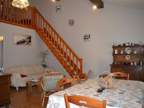 Ein gemütliches Wohnzimmer mit einer Holztreppe, einem Esstisch mit gemustertem Tischläufer und einer Auswahl dekorativer Gegenstände in einer Holzvitrine.
