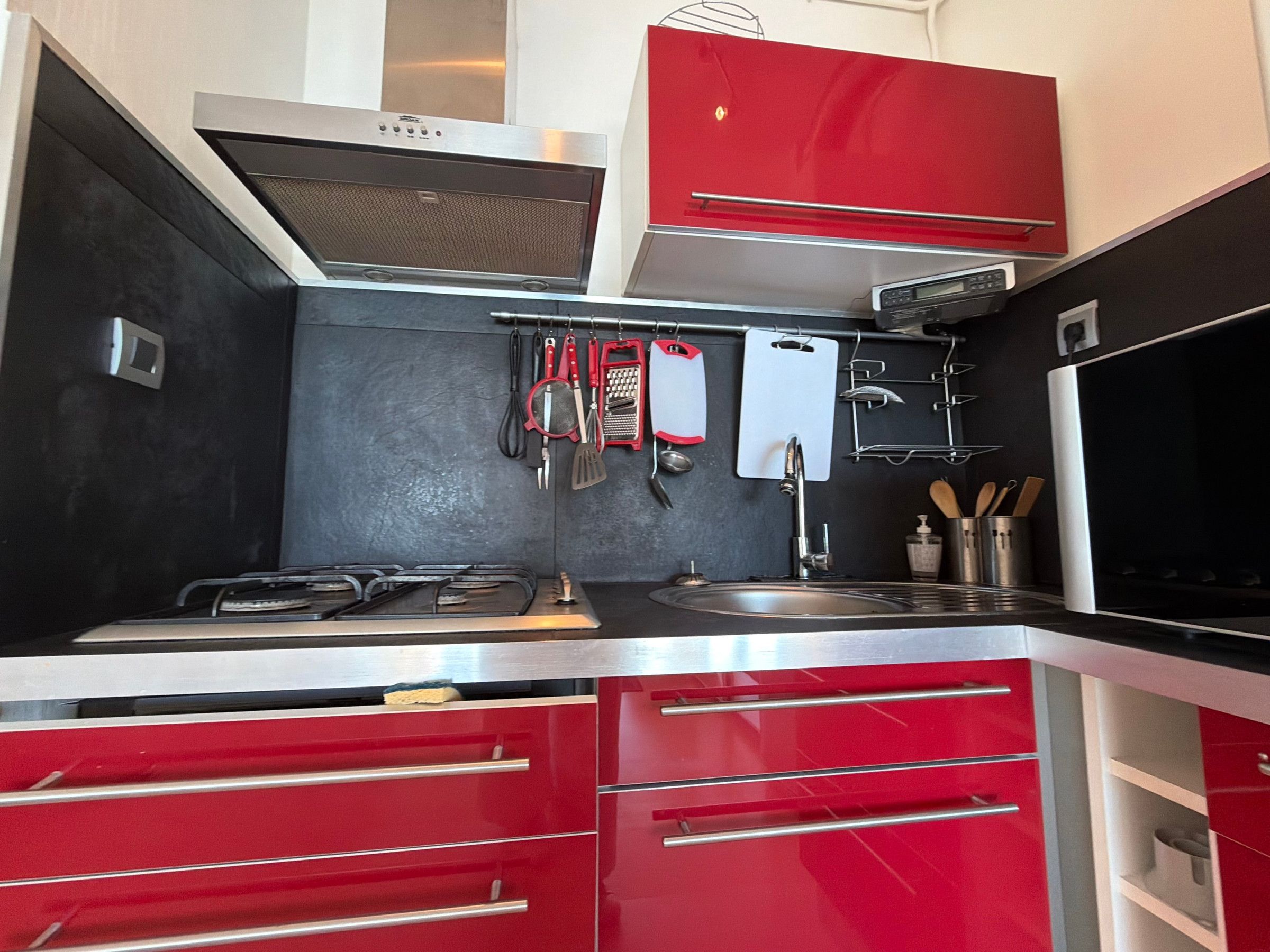 A modern kitchen with red cabinets, stainless steel appliances, and a variety of utensils hanging on the wall.