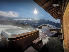 Un bain à remous avec vue sur une montagne enneigée, une structure extérieure en bois et un ciel dégagé.