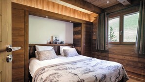A wooden cabin-style bedroom with a bed, pillows, a nightstand, and a window with curtains.