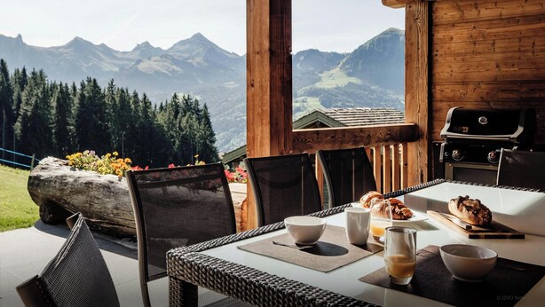 A wooden dining table with chairs, a grill, and a view of mountains.