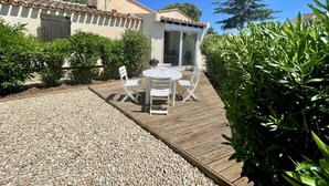 A patio with a table and chairs, a barbecue grill, and a building with a tiled roof and a glass door.
