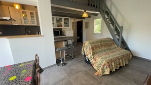 A compact bedroom with a bed, a small table, and a chair. There is a staircase leading to an upper level.