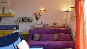 A compact living space with a purple sofa, a small dining table, and a kitchen area with a microwave and a radio. - 3-room villa with air conditioning, parking, and pets allowed in Saint-Pierre-la-Mer (Fleury-Saint-Pierre-la-Mer)