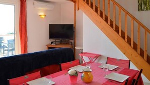 A dining area with a table set for four, a television, and a staircase. - 3-room villa with air conditioning, parking, and pets allowed in Saint-Pierre-la-Mer (Fleury-Saint-Pierre-la-Mer)