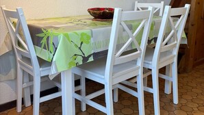 A dining table with a green floral tablecloth, surrounded by white chairs. - Cozy Studio w/ Mezzanine, Terrace, Pool & Parking - Near Beach and Town Center (Fleury-Saint-Pierre-la-Mer)