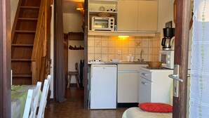 A compact kitchen with a microwave, stove, and sink. There is a small dining area with a table and chairs. - Cozy Studio w/ Mezzanine, Terrace, Pool & Parking - Near Beach and Town Center (Fleury-Saint-Pierre-la-Mer)