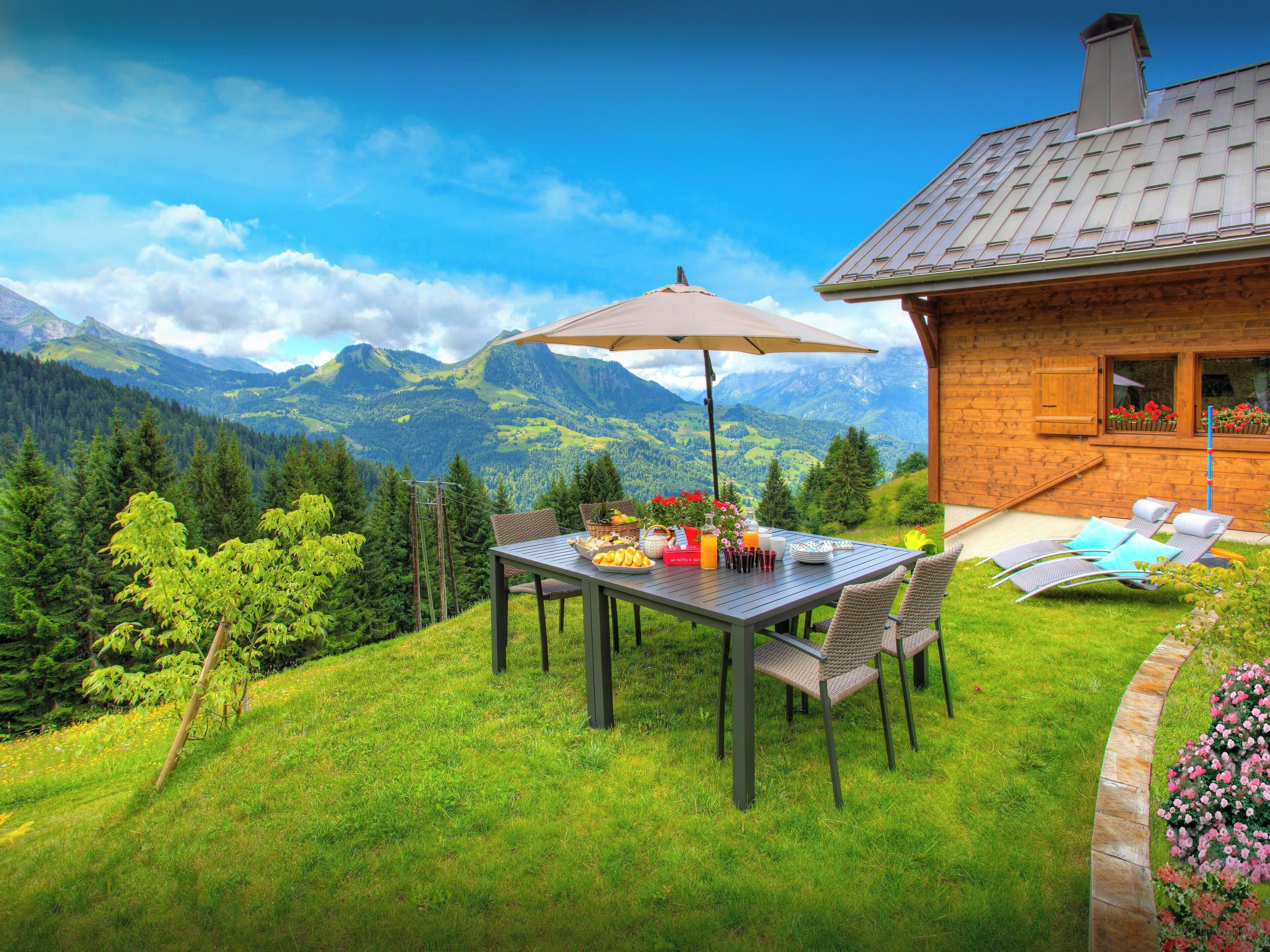 Une table à manger avec des chaises et un parasol, le tout installé devant un paysage montagneux.