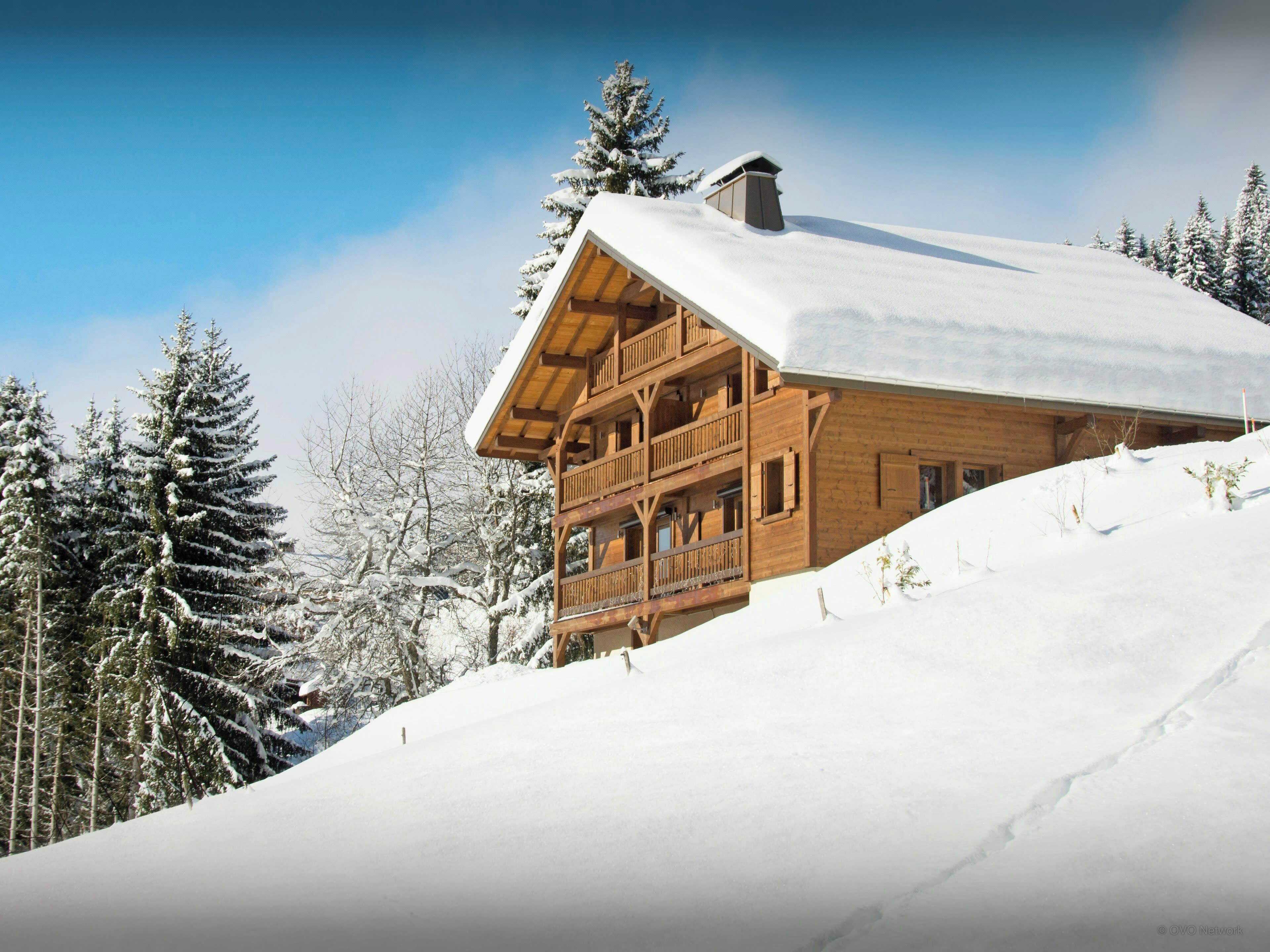 Un chalet en bois doté d’un balcon, entouré d’arbres couverts de neige.