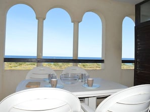 A table set for two with a clear view of the ocean through arched windows.