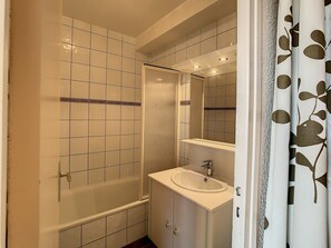 A bathroom with white tiled walls, a bathtub, a sink, and a mirror.
