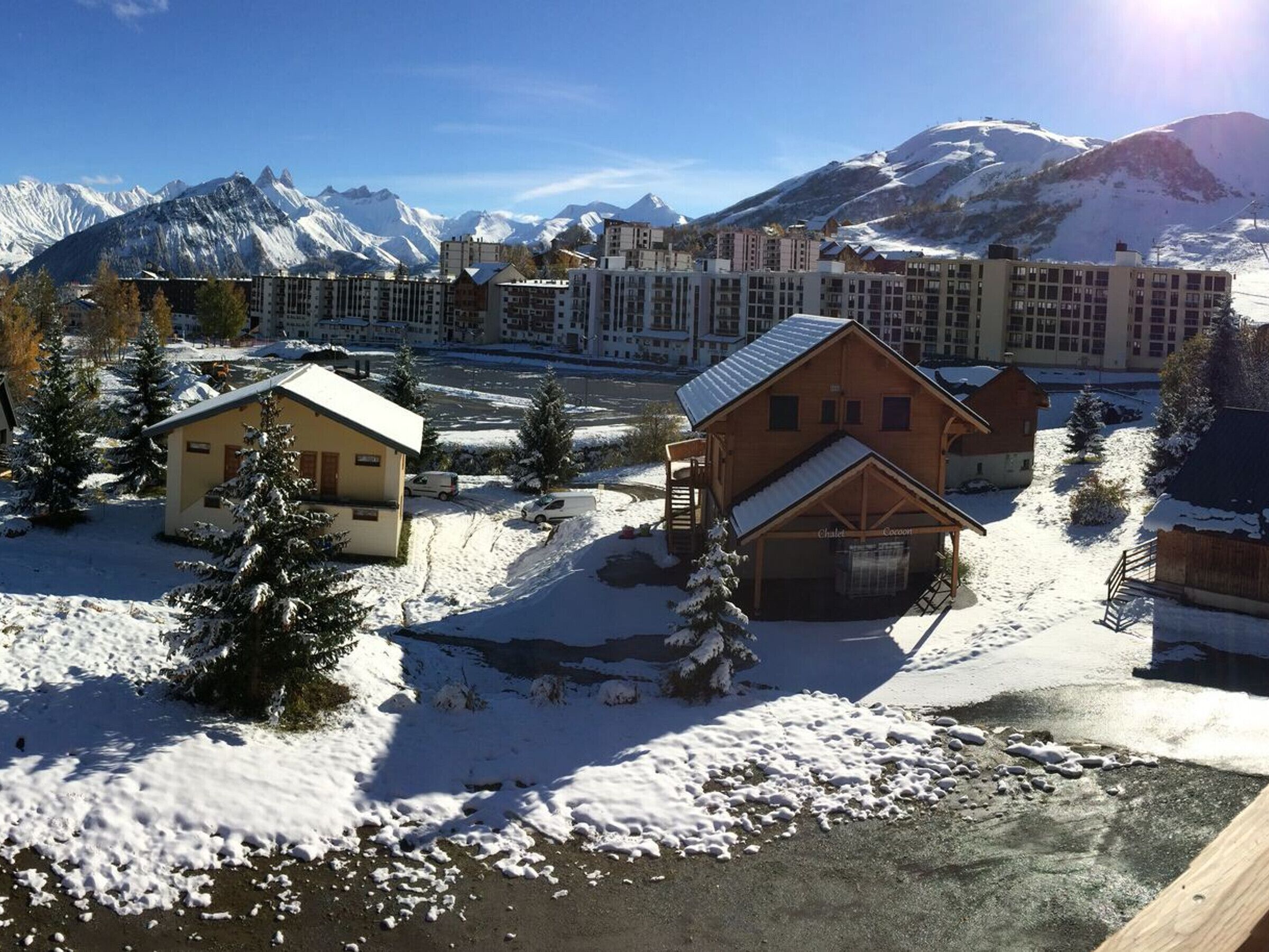 Une station de montagne enneigée, avec des bâtiments de style chalet, une piste de ski et une vue dégagée sur les sommets enneigés en arrière-plan.