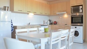 A modern kitchen with white cabinetry, a dining table with chairs, a microwave, an oven, and a washing machine.