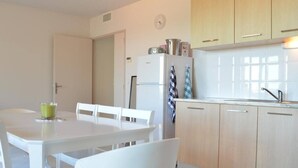 A modern kitchen with white cabinetry, a dining table with chairs, and a refrigerator.