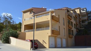 A multi-story building with balconies, a red car parked in front, and a clear blue sky.