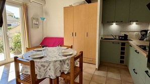 A dining area with a table set for four, a wooden cabinet, and a kitchenette with green cabinets and a stove. - Cozy 2-Room House with Mezzanine, A/C, Parking, Near Beach - Argeles-sur-Mer (Argelès-sur-Mer)