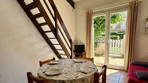 A dining area with a table set for four, a television on a small table, and a staircase leading to a balcony with a view of greenery. - Cozy 2-Room House with Mezzanine, A/C, Parking, Near Beach - Argeles-sur-Mer (Argelès-sur-Mer)